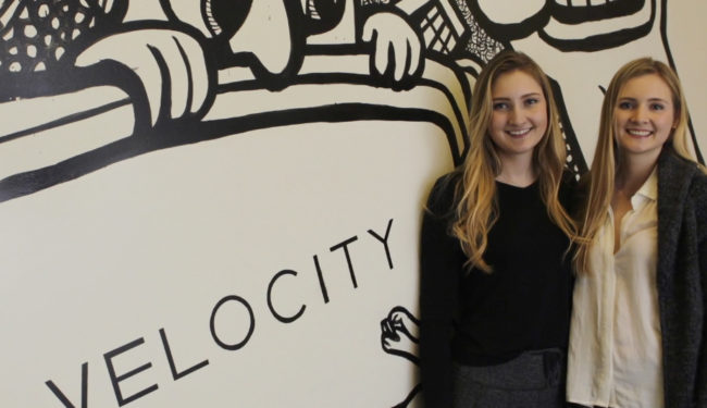 Two people posing in front of the Velocity logo