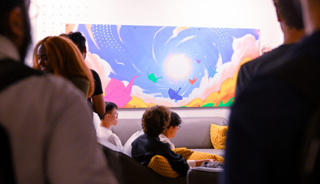 People gathered around colourful wall art with blue, pink and yellow colours.